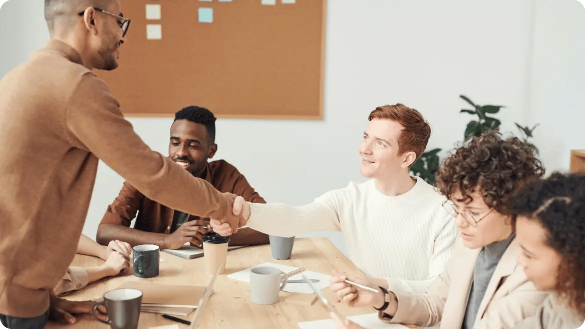 Group of people in a meeting with two individuals shaking hands, representing trusted backup compliance.