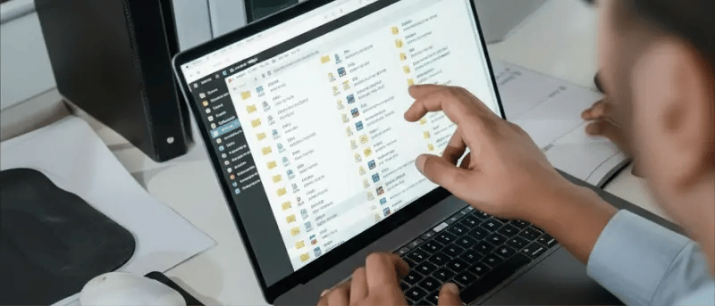 Person pointing at a laptop screen displaying a list of digital documents.