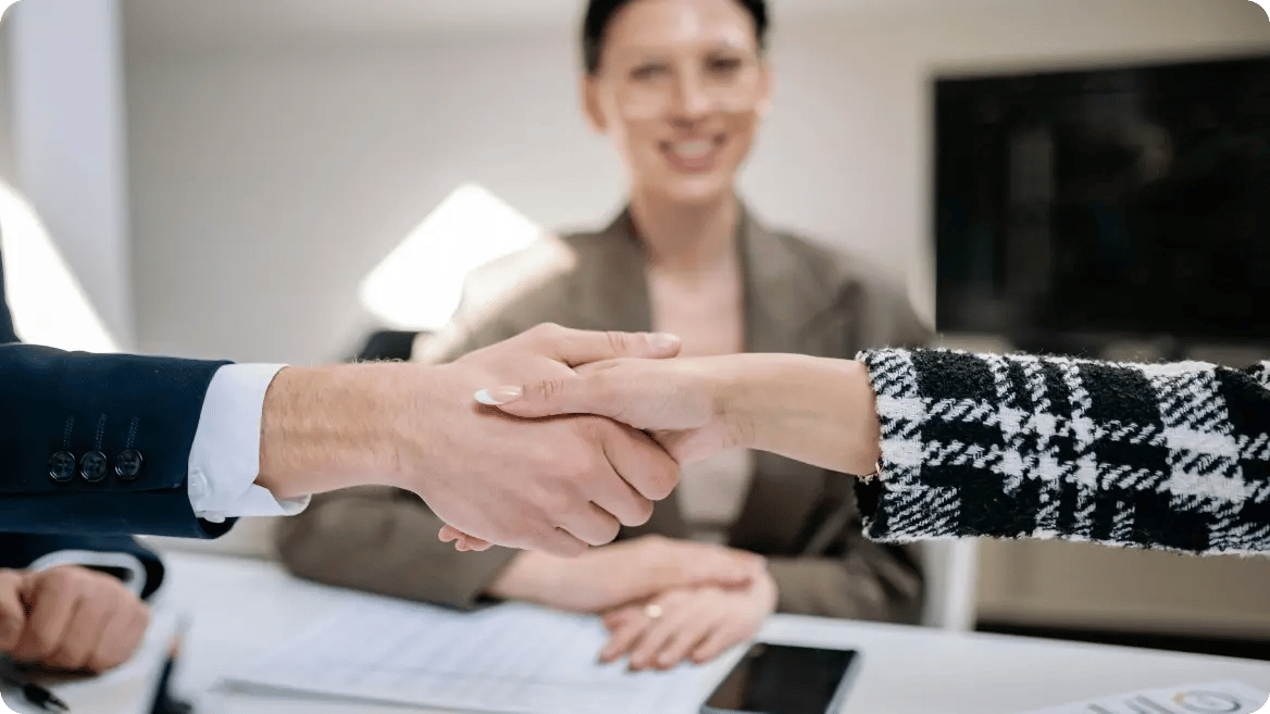 Three people in a meeting with two shaking hands.
