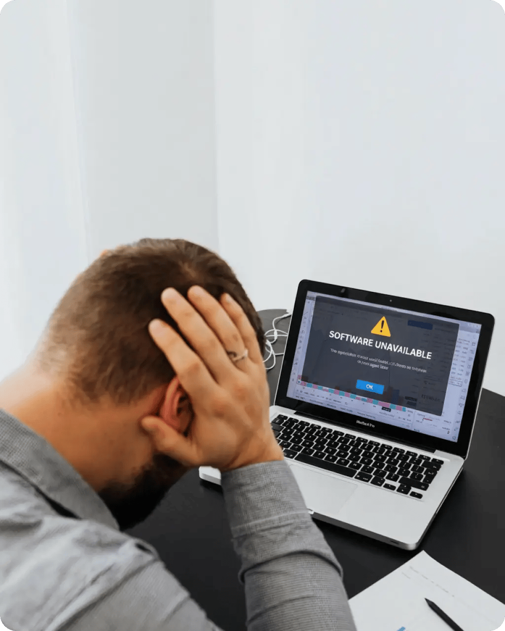 A frustrated person with their hand on their head sitting in front of a laptop displaying a 'Software unavailable' error message.