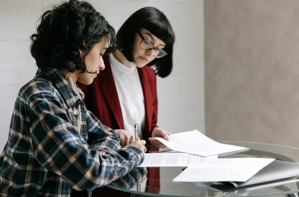 Two women talking over papers on a table, appearing to review or sign documents.