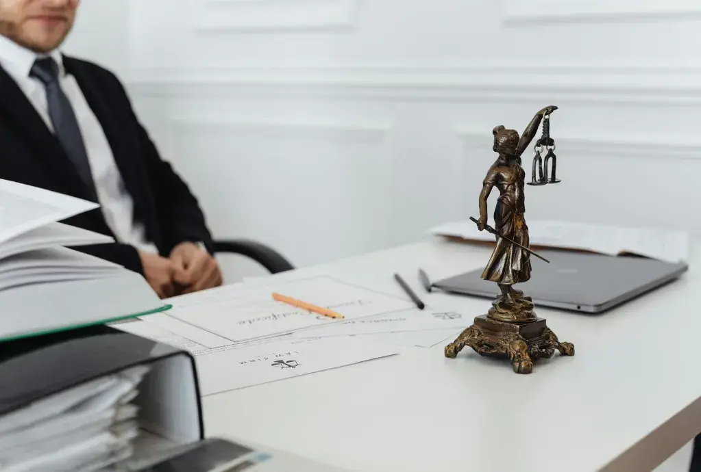 Man sitting at a table with a legal figurine and papers in front of him.